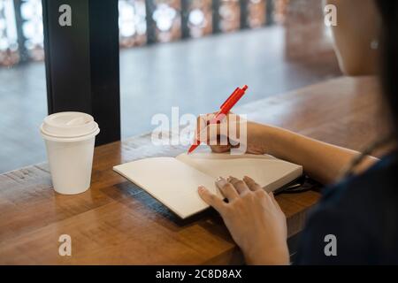 Eine Frau, die im Café mit heißem Kaffee sitzt, das Notizbuch öffnet und ihr Tagebuch schreibt, während sie auf ihren Geliebten als Termin wartet, zugeschnittenes Bild von o Stockfoto