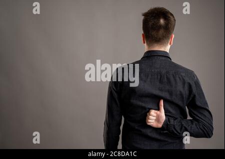 Rückansicht der ernst stilvolle attraktive Mann mit einem lässigen schwarzen Hemd gekleidet zeigt Finger gekreuzt isoliert auf grauem Hintergrund mit Kopieplatz adve Stockfoto