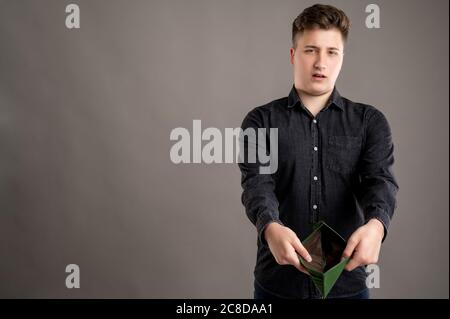 Portrait von ernst stilvolle attraktive Mann mit einem lässigen schwarzen Hemd gekleidet zeigt leere Brieftasche isoliert auf grauem Hintergrund mit Copy-Raum-Werbung Stockfoto