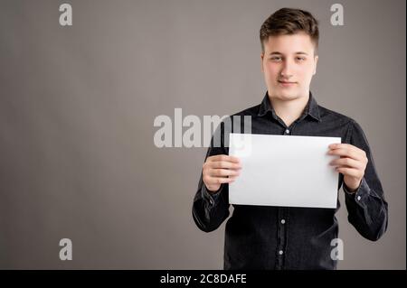 Portrait von ernst stilvolle attraktive Mann mit einem lässigen schwarzen Hemd mit weißem Papier isoliert auf grauem Hintergrund mit Copy-Raum Werbung gekleidet Stockfoto