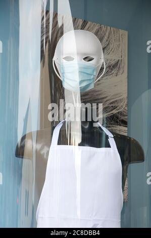 Finstere maskierte Schaufensterpuppe mit PSA (persönliche Schutzausrüstung), im Fenster eines Friseursalons, während der Coronavirus-Pandemie. England. Stockfoto