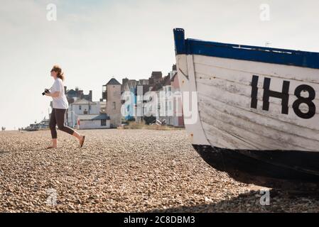 Kamerafotografie einer jungen Frau, Ansicht einer jungen Frau, die eine Kamera hält und alleine an einem Strand in Aldeburgh an der Küste von Suffolk, England, Großbritannien, spaziert Stockfoto
