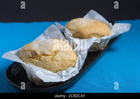 Zwei hausgemachte Muffins in Papier auf einer blauen Matte eingewickelt und der Hintergrund ist dunkel Stockfoto