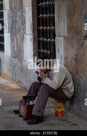 Damaskus, Syrien 03/28/2010: Ein armer junger Syrer in zerrissenen Kleidern sitzt auf einer leeren Dose vor seinem Schuhputzstand. Er beißt Stockfoto