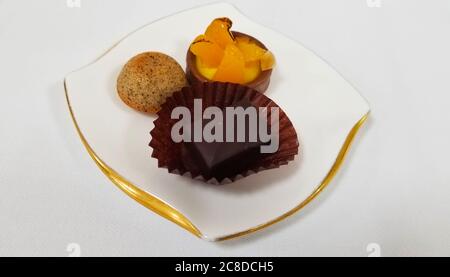 Ein dekorativer Dessertteller aus Porzellan mit goldenen Rändern. Darauf gibt es einen kleinen Obstkuchen, einen Kuchenball und ein Stück Schokolade Stockfoto