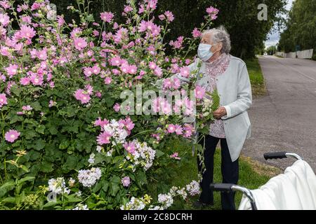 Eine alte Frau im Rollstuhl, in einer medizinischen Maske auf einem Spaziergang im Garten mit Blumen. Hochwertige Fotos Stockfoto