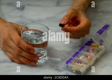 Frau erreicht eine Pillenbox mit Medikamenten für jeden Tag. Nützliche Demonstration für chronische Krankheiten, Multi-Drogen- oder Ergänzungsgebrauch Stockfoto