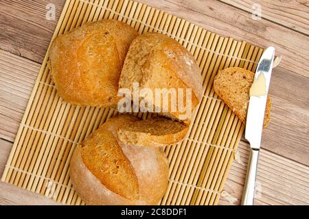 Nahaufnahme Bild von hausgemachten Vollkornbrot Brote frisch aus dem Ofen. Sie kühlen auf einer Bambusmatte auf einem Holztisch. Ein Buttermesser mit Butter. Stockfoto