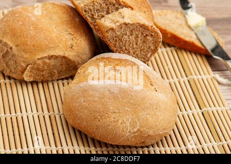 Nahaufnahme Bild von hausgemachten Vollkornbrot Brote frisch aus dem Ofen. Sie kühlen auf einer Bambusmatte auf einem Holztisch. Ein Buttermesser mit Butter. Stockfoto