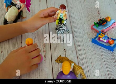 Kind spielt mit Spielzeugfiguren auf Holztisch. Sie schafft eine Komposition aus tierischen und menschlichen Figuren und spielt eine Geschichte aus ihr heraus, indem sie sich bewegt Stockfoto