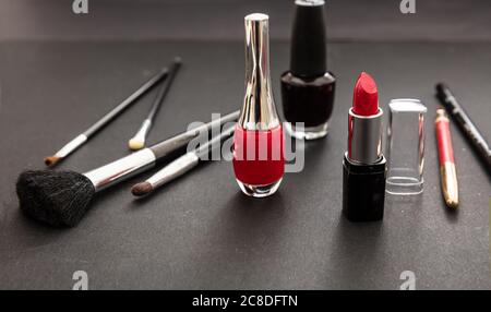 Kosmetikprodukte in Rot und Schwarz herstellen. Roter Lippenstift und nagellack, Augenstift und Bürsten vor schwarzem Farbhintergrund Stockfoto