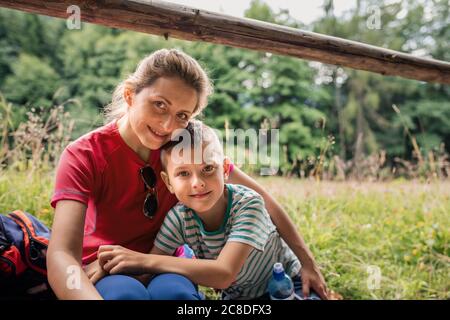 Porträt einer lächelnden Mutter und ihres niedlichen Sohnes auf einem Pfad sitzen, eine Pause von ihrer Familie Wanderung Stockfoto