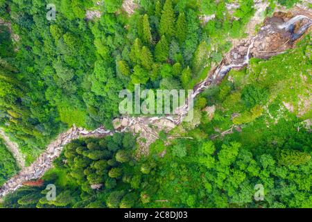 Bergbach mit einem Wasserfall auf besagter fließt zwischen einem dichten Wald von Nadelbäumen und Laubbäumen, Top Luftbild Stockfoto