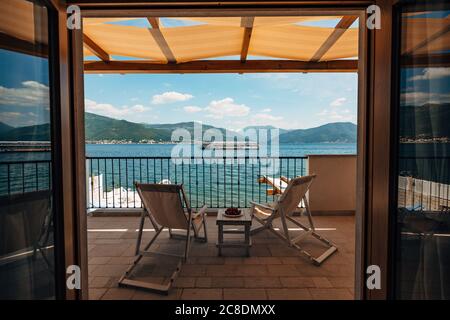 Zwei Sonnenliegen auf dem Balkon des Hotelzimmers mit Blick auf das Meer und ein vorbeifahrenden Touristenboot. Stockfoto