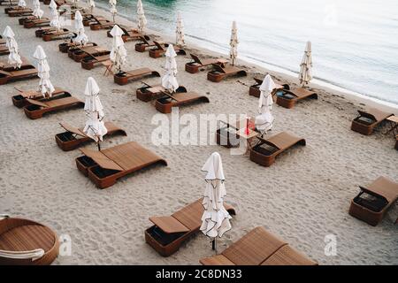 Braune Plastikliegekörben mit Sonnenschirmen am Sandstrand. Stockfoto