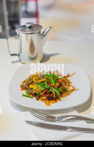 Teller gebratene Nudeln mit Gewürzen, frischem Gemüse, Sojasauce und grünem Tee im Wasserkocher Stockfoto