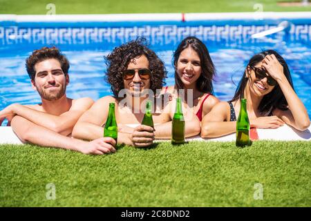 Lächelnde junge multiethnische Freunde mit Bierflaschen genießen den Sommer in Swimmingpool im Hinterhof Stockfoto