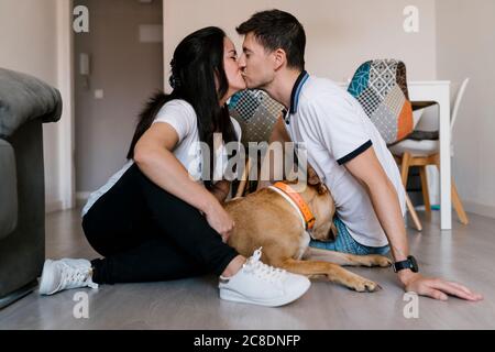 Paar küssen sich gegenseitig während sitzen von Hund auf dem Boden Zu Hause Stockfoto