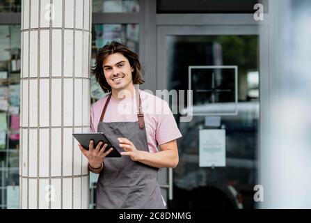 Lächelnder Besitzer, der ein digitales Tablet benutzt, während er an der Säule ansteht Café Stockfoto