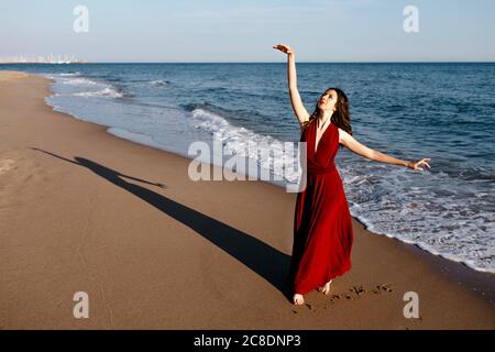 Zarte Frau in rotem Kleid tanzen am Meer, die Sonne fühlen Stockfoto