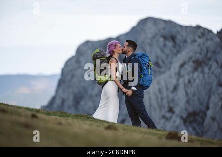 Küssendes Brautpaar mit Kletterrucksäcken am Urkiola Berg, Spanien Stockfoto