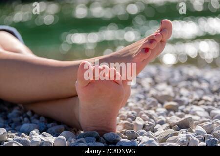 Junge Frau mit barfuß sitzt auf Kieselsteinen am Flussufer Stockfoto