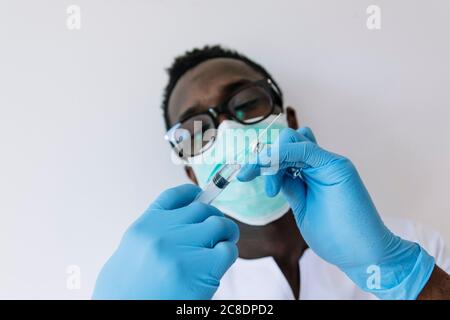 Nahaufnahme eines Afroarztes, der Spritze und Fläschchen gegen Weiß hält Hintergrund Stockfoto