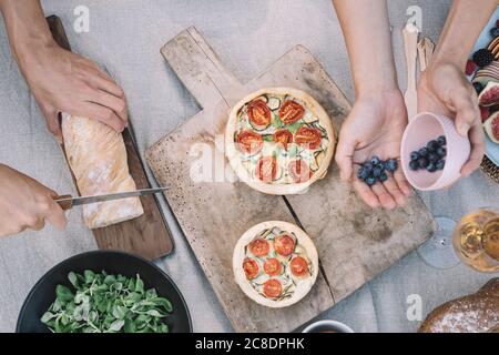 Hände der Frau, die Heidelbeeren, während Freund schneiden Brot auf Tabelle Stockfoto