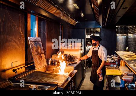 Koch trägt Schutzmaske Vorbereitung Grill in Restaurant Küche Stockfoto