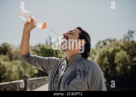 Nahaufnahme eines reifen Mannes, der Wasser trinkt, während er gegen klar steht Himmel im Park Stockfoto