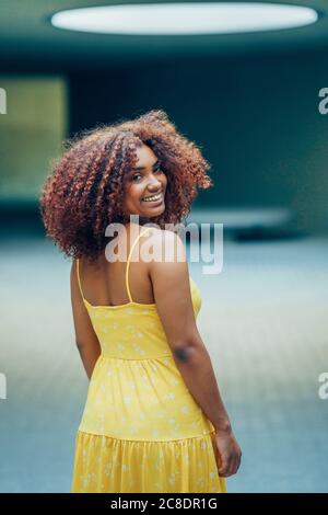 Lächelnde junge Frau in gelbem Kleid, die drinnen steht Stockfoto