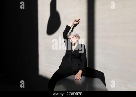 Stilvolle Geschäftsfrau trägt eleganten Anzug mit geschlossenen Augen sitzen auf Haltewand Stockfoto