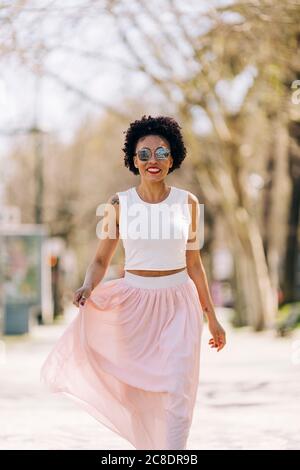 Stilvolle Frau trägt Sonnenbrille beim Gehen auf dem Fußweg Stockfoto