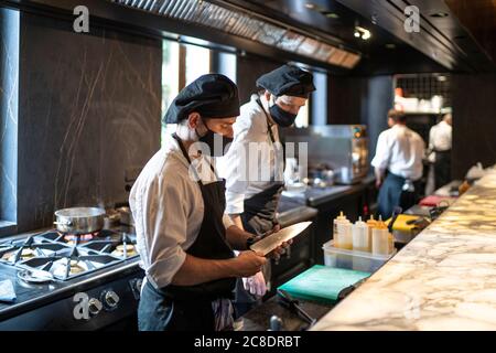 Köche tragen Schutzmasken und arbeiten in der Restaurantküche zusammen Stockfoto