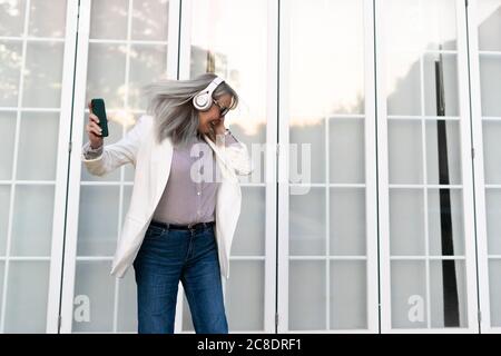 Ältere Unternehmerin tanzt beim Hören von Musik über Kopfhörer gegen Bürotür Stockfoto