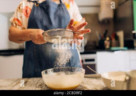 Nahaufnahme einer Bäckerin, die Mehl im Teig auf dem Tisch gesiebt hat In der Werkstatt Stockfoto