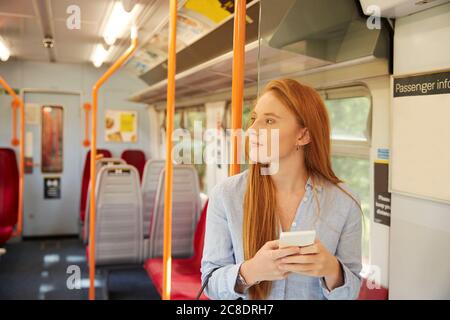 Nachdenkliche Frau hält Smartphone, während sie im Zug steht Stockfoto