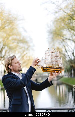 Geschäftsmann hält Modellschiff an einem Kanal Stockfoto