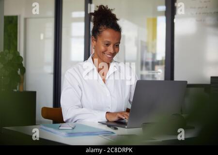 Porträt einer lächelnden Geschäftsfrau, die im Büro am Laptop arbeitet Stockfoto