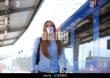 Junge Frau trägt eine schützende Gesichtsmaske, während sie bei der Eisenbahn läuft Station Stockfoto