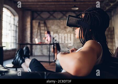 Junge Frau entspannt in Sessel im Loft Büro tragen VR Schutzbrille Stockfoto