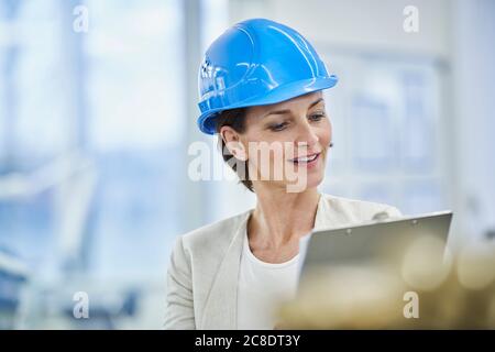 Reif weiblich Manager in blau hardhat Lesung Zwischenablage in der Fabrik Stockfoto