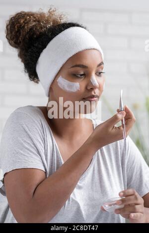 Nahaufnahme der jungen Frau trägt Stirnband Anwendung Gesichtsmaske mit Bürsten Sie zu Hause Stockfoto