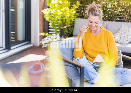 Portrait einer lächelnden reifen Frau, die auf der Terrasse sitzt und Heidelbeeren isst Beim Lesen eines Buches Stockfoto