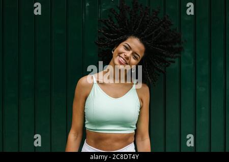 Glückliche junge Frau wirft ihre schwarzen Locken gegen grünes Metall Tür Stockfoto