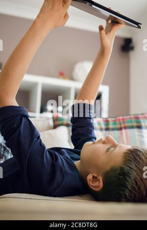 Junge Spiele auf dem digitalen Tablet, während er auf dem Sofa liegt Zu Hause Stockfoto