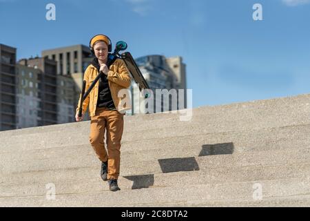 Junge, der Push-Roller trägt, während er auf Stufen gegen nach unten geht Blauer Himmel Stockfoto