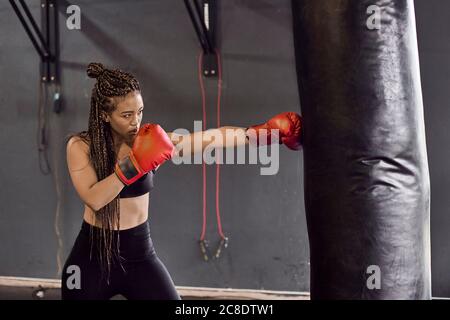 Boxerin trägt rote Handschuhe und übt Boxbohrer beim Stanzen Tasche im Fitnessstudio Stockfoto