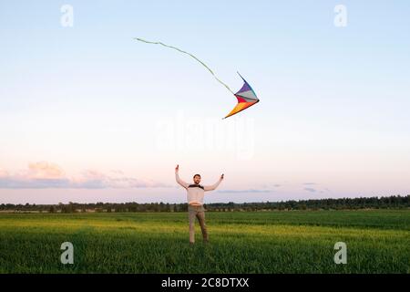 Mittelerwachsener Mann, der Drachen fliegt, während er auf einer grasbewachsenen Landschaft steht Gegen den Himmel bei Sonnenuntergang Stockfoto