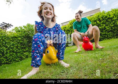 Glückliche Geschwister spielen mit hoppity Pferde auf grasbewachsenen Land in Hof Stockfoto